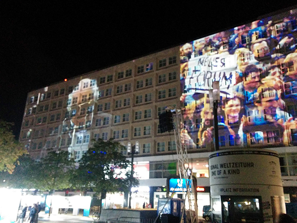 People celebrating the 30th anniversary of the fall of the Berlin Wall illuminated on a building in the city’s Alexanderplatz public square, located near the site of QWS2019.