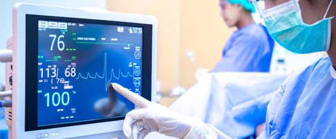 Medical professional's gloved hand points to a monitor displaying patient vital signs.