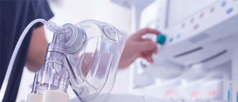 Clear oxygen mask in foreground, hand adjusting medical equipment.