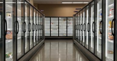 Empty or sparsely stocked grocery store refrigerator aisle with glass display cases.