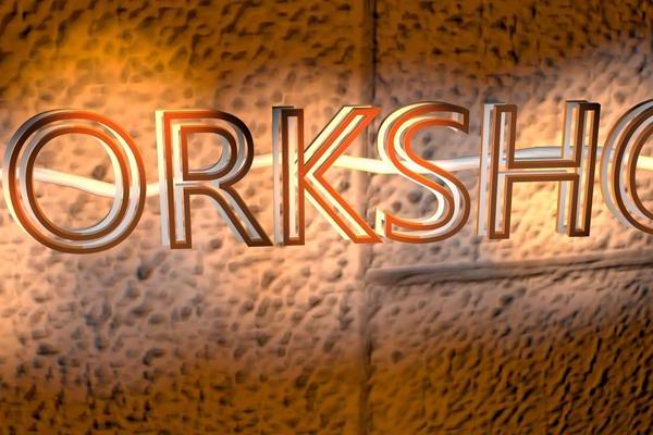 WORKSHOP text in glowing orange neon on a textured brown wall.